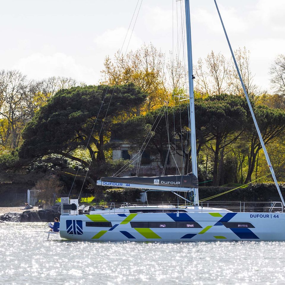 Side view of a Dufour 44 sailing monohull at anchor near scenic shoreline